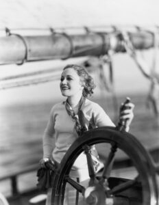 Young woman holds the steers the wheel of a sailing ship